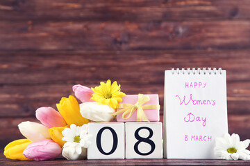 Text Happy Womens Day with tulip, chrysanthemum flowers and gift box on brown wooden background