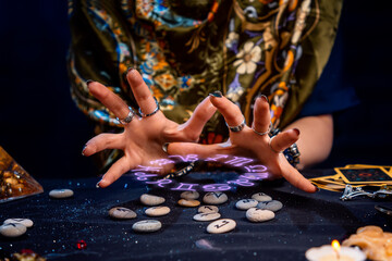 The female hands of the soothsayer read the runes. The zodiac circle glows above the runes. Close up. The concept of divination, astrology and predicting the future