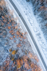 Aerial view from drone of car on a curvy snow covered road in the winter forest
