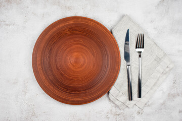 Empty plate and cutlery on a napkin. Dinner setting, ceramic plate and silverware over light table...