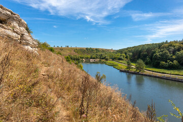 Fototapeta na wymiar View of the Vorgol River with a dam in the distance and a rocky bank in the former estate of the merchant Taldykin near the city of Yelets, Lipetsk region, Russia