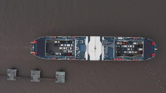 Overhead top down aerial drone shot of car ferry leaving docks fully loaded seagulls swarming
