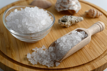 Fototapeta na wymiar Little wooden scoop and glass bowl full of sea salt on wooden cutting board on white background