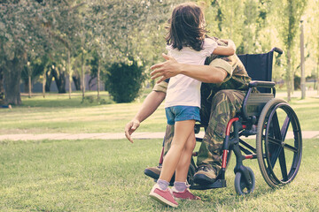Disabled retired military man meeting and hugging little daughter in park. Veteran of war or...