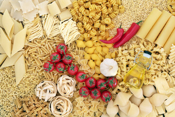 Italian pasta assortment & food ingredients of tomatoes, garlic, olive oil & red chilli peppers. Flat lay, top view.