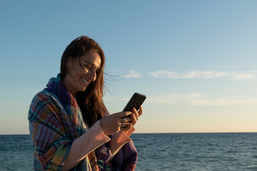 woman using her smartphone on a cold day at the beach