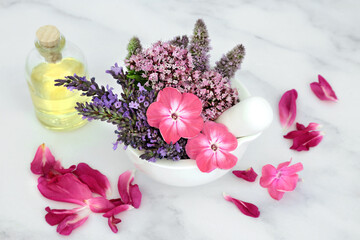 Natural herbal medicine with  flowers and herbs in a mortar and  pestle with oil bottle and rose petals on marble. Still life for naturopathic health care for aromatherapy essential oil preparation.