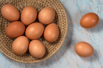 several fresh chicken eggs in a straw basket on a wooden background. Healthy eating concept.