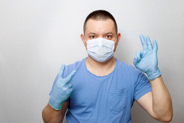 Portrait of young doctor in mask and gloves ok sign isolated on grey background.