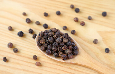 Fototapeta na wymiar Heap of black peppercorns on a wooden spoon with some scattered around