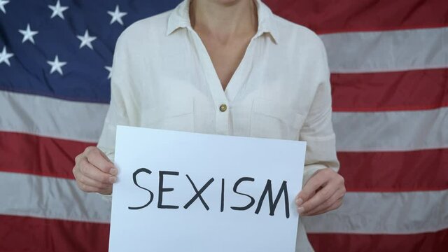 Sexism. Woman on the background of the flag of america with sexism posters.