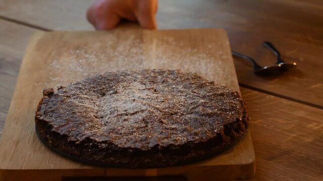 Person serving and presenting a home baked chocolate cake, a classic traditional Swedish cake called Kladdkaka, on a rustic wooden cutting board.