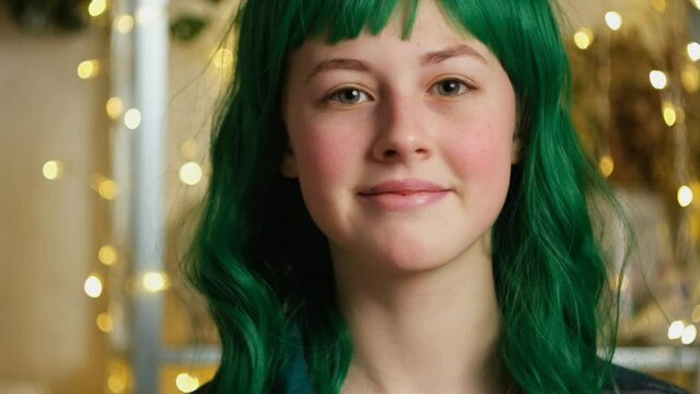 Portrait of beautiful teen caucasian girl with coloured green hair. Attractive girl smiling indoors, golden bokeh lights on background.