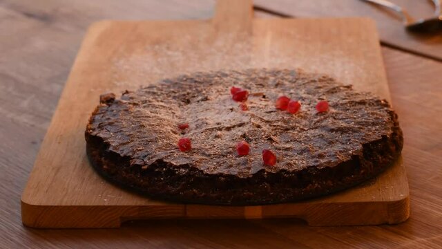 Fresh pomegranate seed sprinkled over a home baked chocolate cake served on wooden cutting board. The chocolate cake is a classic Swedish dessert called Kladdkaka.