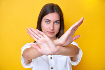 Brunette girl showing stop gesture with hands, looking at the camera with strong face isolated on...