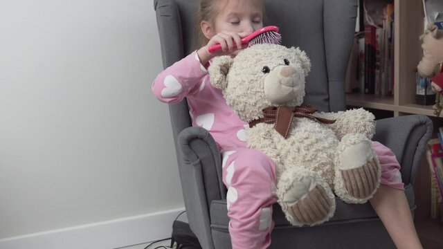 A little girl combs a toy teddy bear.