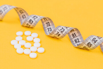 White measuring tape with a white pills, white vitamin on a yellow background. Diet. Slimming....