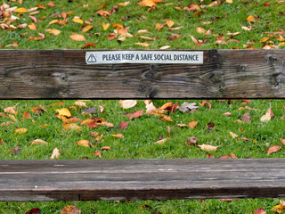 A message taped to the back rest of an outdoor wooden bench says 'please keep a safe social distance'. Guidance given due to global Covid 19 pandemic.
