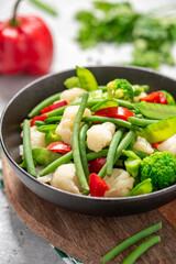 Cooked vegetables in a plate close-up. Steamed bean pods, pea pods, cauliflower, broccoli, and peppers. Healthy diet food, vegan food.