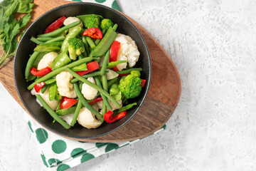 Cooked vegetables in a plate on a gray background top view. Copy space for text. Steamed bean pods, pea pods, cauliflower, broccoli, and peppers. Healthy diet food, vegan food.
