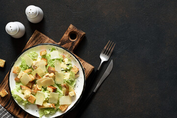 Fototapeta na wymiar Caesar salad in a plate on a wooden board on a dark background, top view.