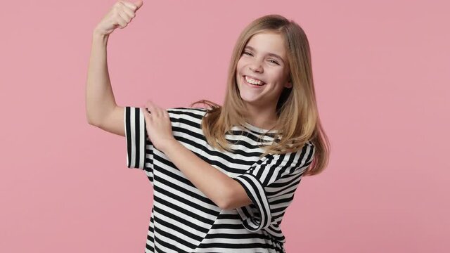 Excited strong little blonde kid girl 12-13 years old wearing white black striped casual t-shirt isolated on pastel pink background studio. Childhood lifestyle concept. Showing biceps muscles on hands