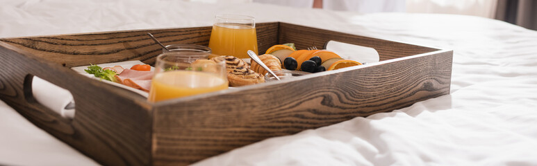 Tasty breakfast on wooden tray on white bedding in hotel, banner