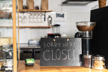 Fototapeta na wymiar Closed sign board on the bar counter in an empty coffee shop. Cafe, bar closed due outbreak lockdown. Small business crisis concept