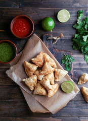 Samosa - fried/baked pastry with filling, popular Indian snacks, served in bowl with spices and fresh cilantro on rustic background