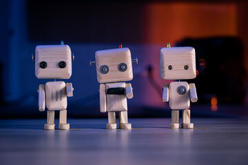 Three small wooden toy robots stand on a table. Photo taken in dark blue tones, in low light.