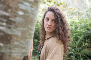 Naklejka premium portrait of a joiven woman in nature. Trees and plants are seen. He is wearing a brown sweater.