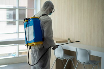 Health care worker in PPE protective suit spraying to disinfect the virus pandemic in the office