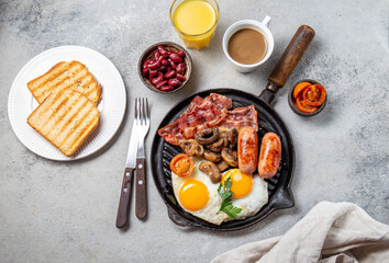 English Breakfast with fried eggs, sausages, bacon, beans, toasts, tomatoes and mushrooms on grill...