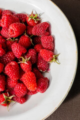 Delicious ripe raspberries from garden lie in white plate.