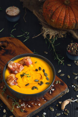 Creamy pumpkin soup with sauteed bacon slices with cream and pumpkin seeds in a black bowl on a black wooden table. Top view, selective focus. Ingredients for making seasonal pumpkin soup on the table