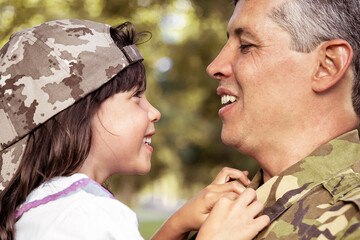 Happy positive father holding little daughter in arms, hugging girl and talking to her outdoors after returning from military mission trip. Closeup shot. Family reunion or returning home concept