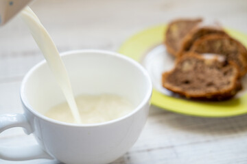 Milk is poured into a cup. Morning breakfast with a muffin.
