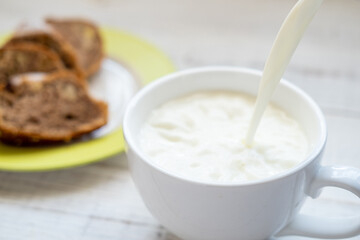 Milk is poured into a cup. Morning breakfast with a muffin.