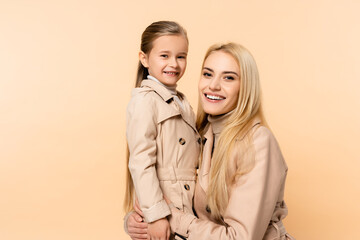 cheerful blonde mother hugging happy daughter isolated on beige