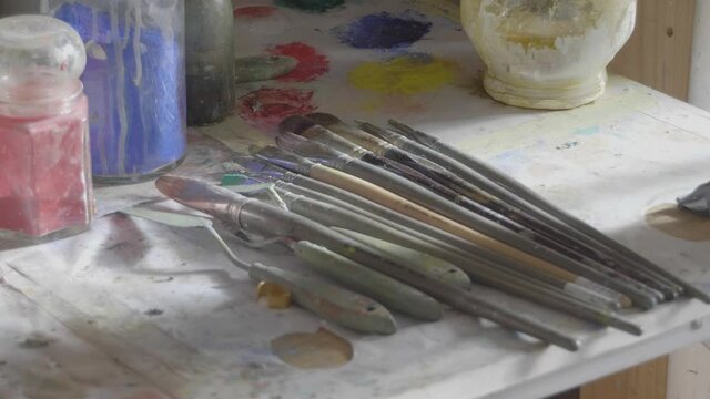 pot of ushes sitting on a table surrounded by paint in and artist's chaotic  studio in the sun