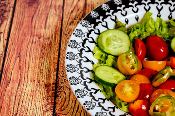 Fresh two-color cherry tomato salad, lettuce, red onion and hot chili served in a vintage bowl on a table. Space for writing. 45 deg. view. close-up.