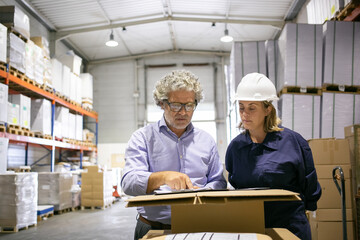 Safety inspector consulting female logistic worker while completing form in warehouse. Copy space,...