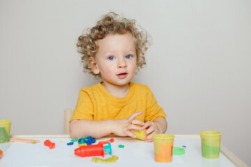 Cute Caucasian blond curly baby boy child playing with sensor kinetic toy playdough. Hand brain...