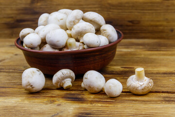Fresh champignon mushrooms in ceramic bowl on the wooden table
