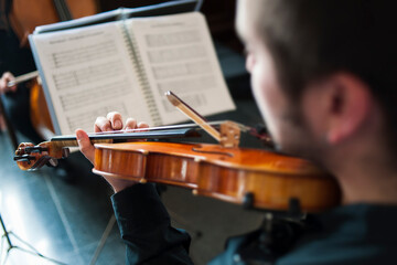 Un hombre toca el violin en una orquestra mirando las partituras.