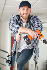 happy male builder standing on ladder with drill