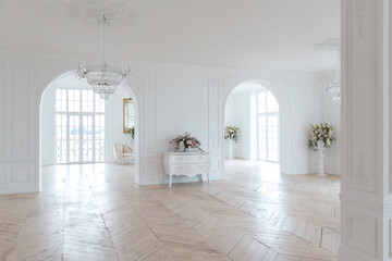 chic white huge spacious hall with a minimum of expensive antique furniture. Baroque interior design with ornament on the walls and parquet on the floor.