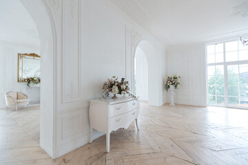 chic white huge spacious hall with a minimum of expensive antique furniture. Baroque interior design with ornament on the walls and parquet on the floor.