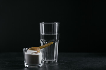 Collagen powder in bowl, glass of water and measure spoon on black background. Extra protein intake. Natural beauty and health supplement concept.
