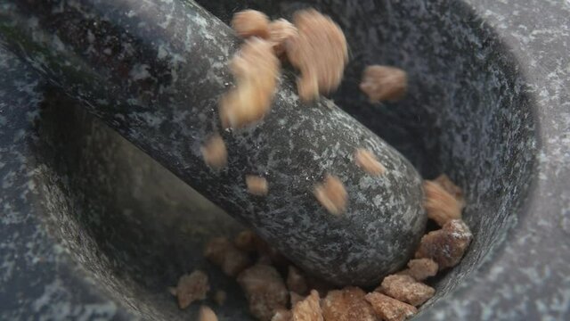 Large pieces of the sweet brown sugar are falling into the grey stone mortar in slow motion